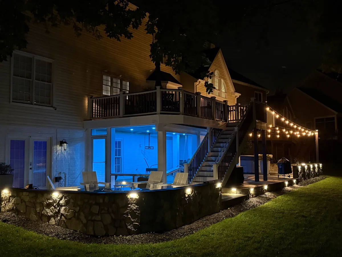 Elevated multi-level deck lit at night with string lights, stair lighting and a glowing screened area below in Northern Virginia